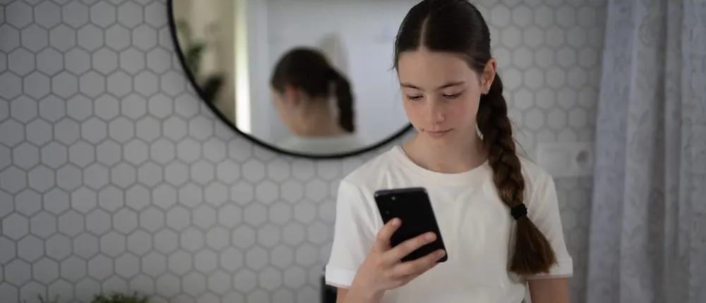 Teenage girl standing in a bathroom looking down at her phone