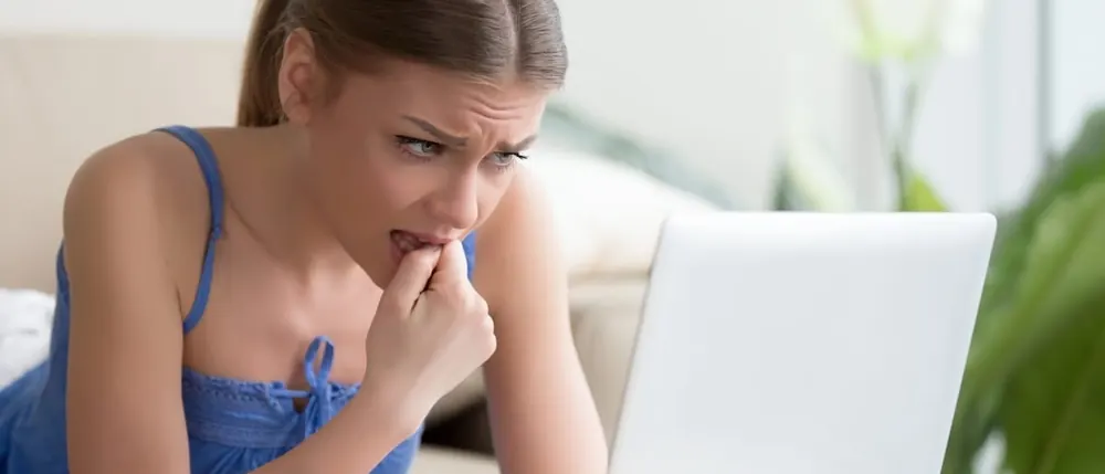 Worried young woman biting her nails while looking at a laptop