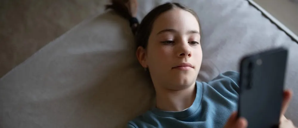 Teenage girl lying on a couch scrolling on her phone